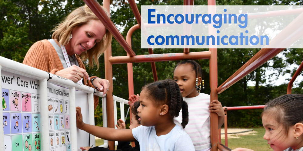 Children and a staff member using a picture-and-word communication board on a playground.