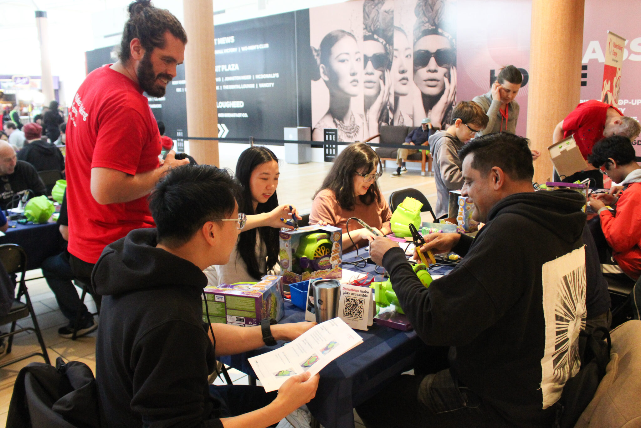 Volunteers working together on toys and switches at a crowded workshop table.