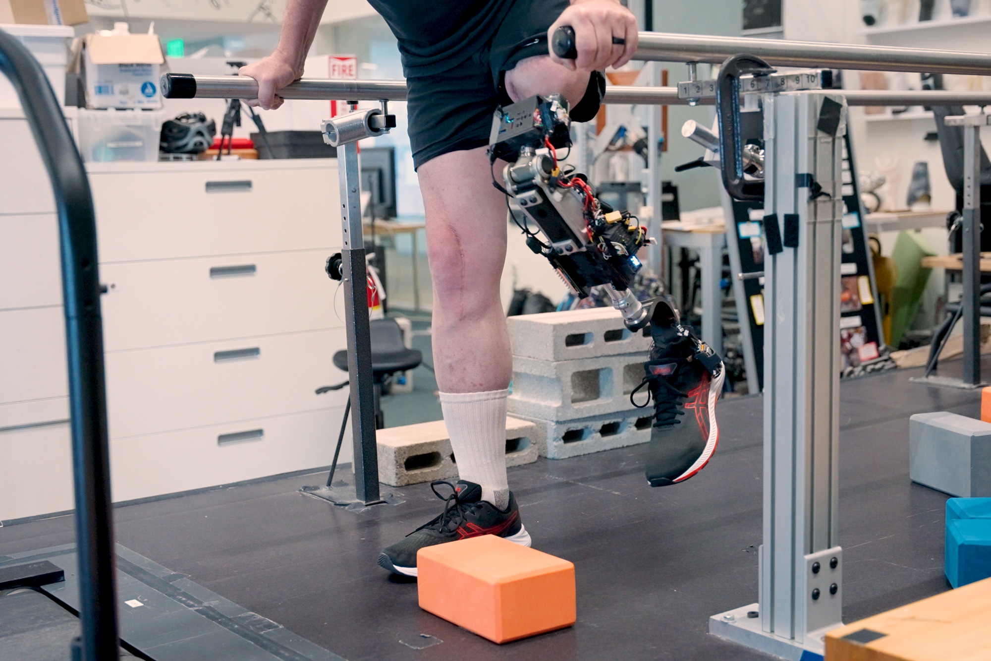 A study participant using an experimental prosthetic leg to step over obstacles between parallel bars.